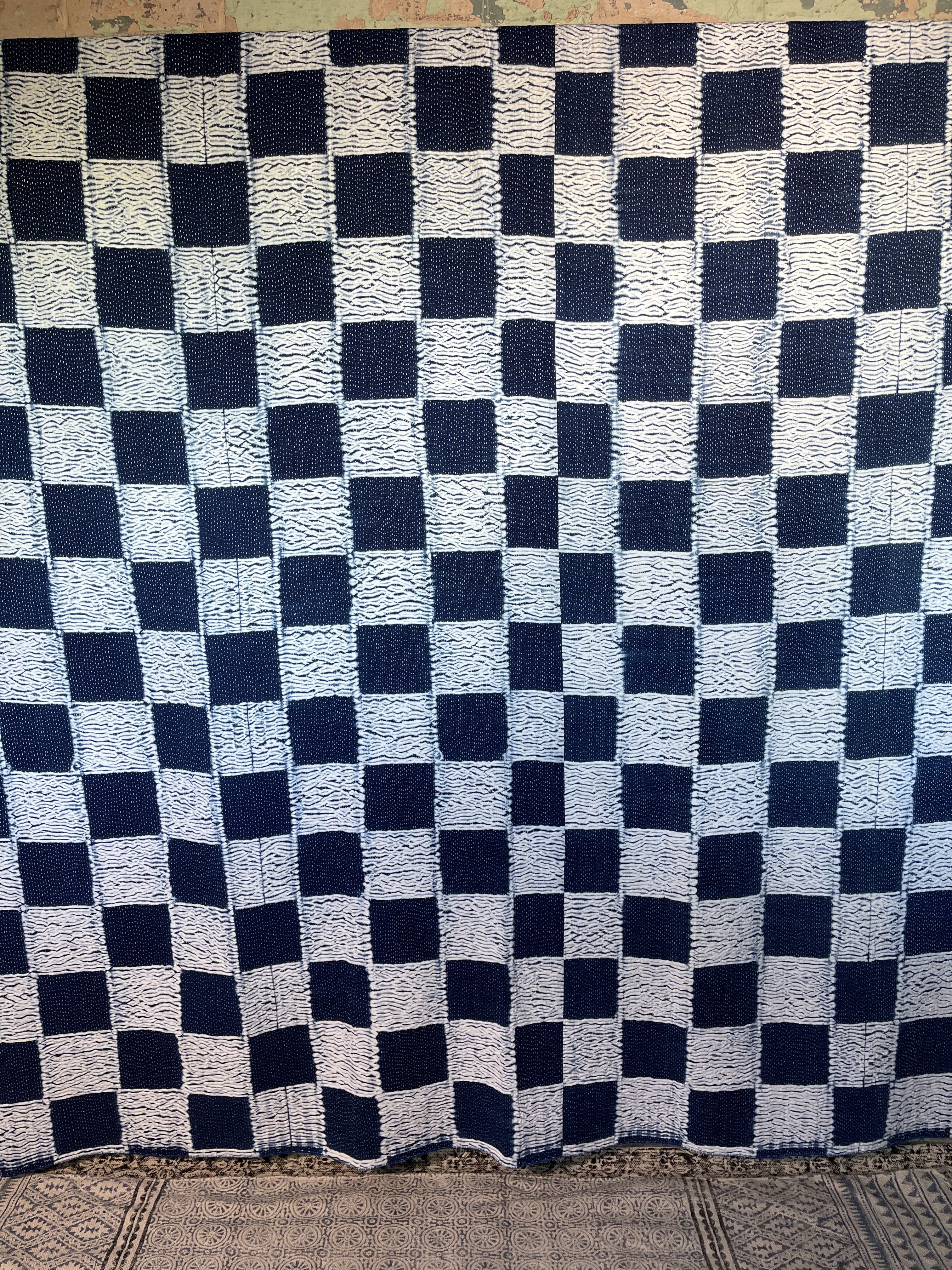 A sunningly beautiful indigo shibori kantha quilt, made by the artisans of LIVING BLUE. The front a check pattern, the reverse showing fine white hand stitiching on a plain indigo background.