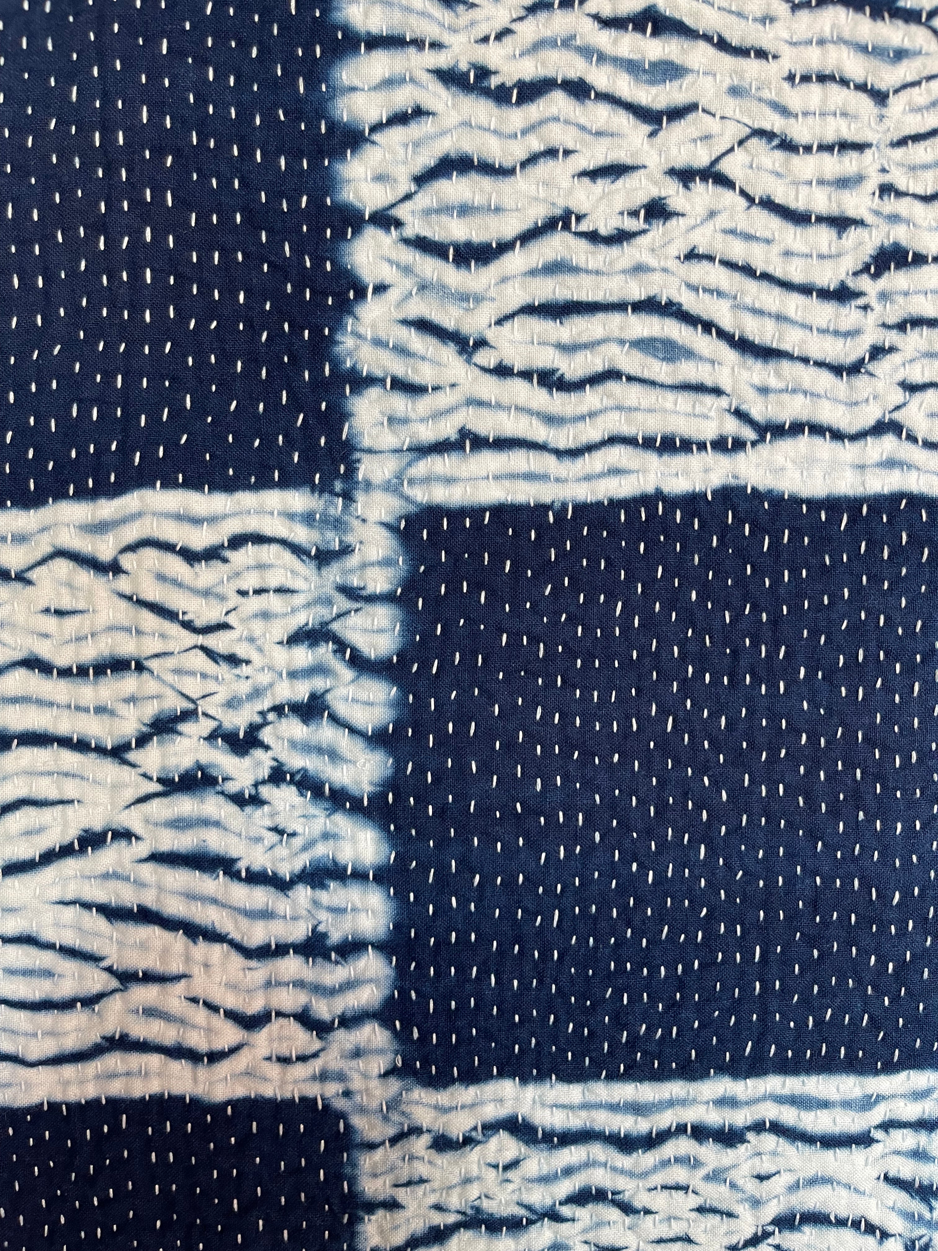 A sunningly beautiful indigo shibori kantha quilt, made by the artisans of LIVING BLUE. The front a check pattern, the reverse showing fine white hand stitiching on a plain indigo background.