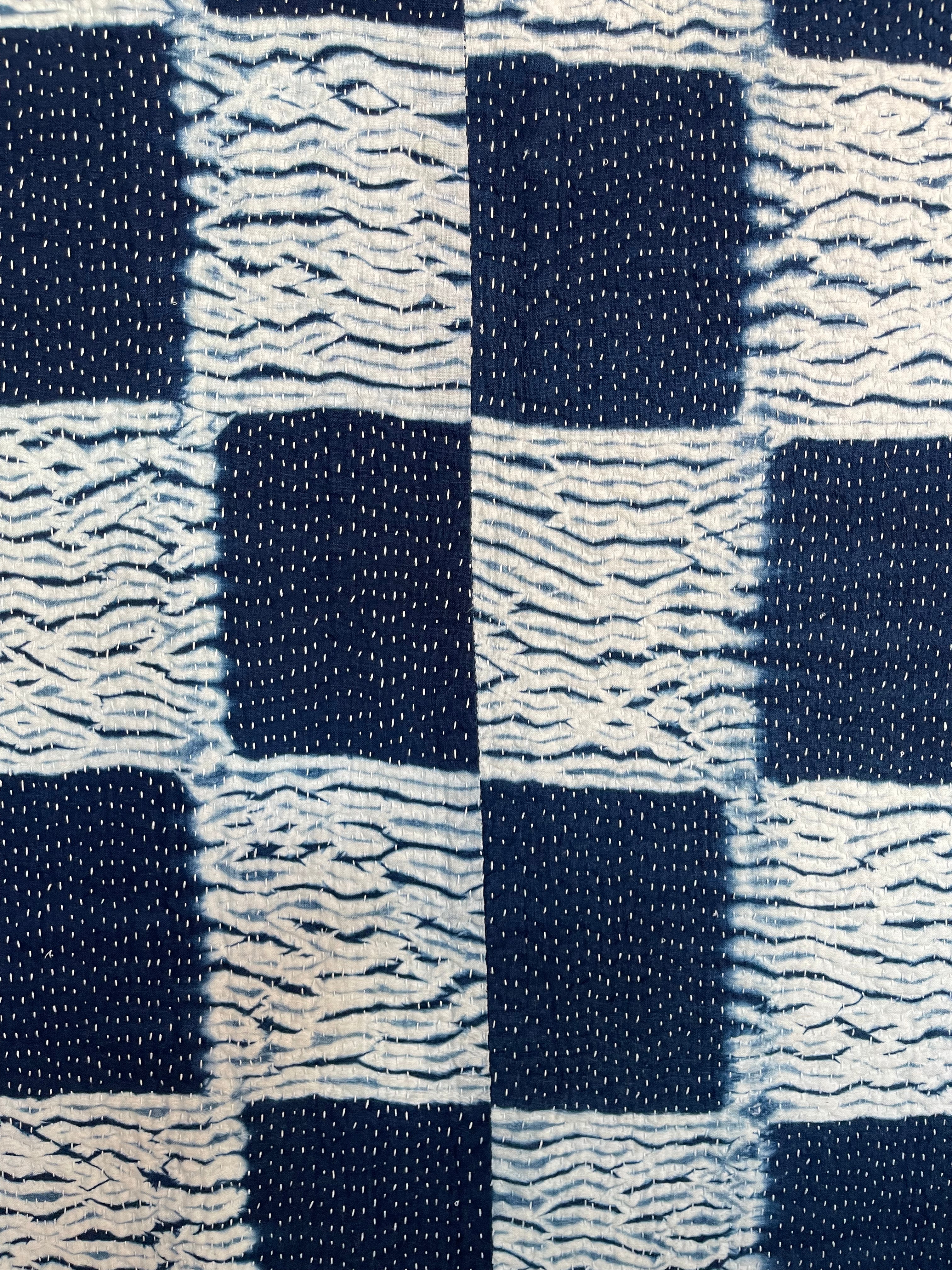 A sunningly beautiful indigo shibori kantha quilt, made by the artisans of LIVING BLUE. The front a check pattern, the reverse showing fine white hand stitiching on a plain indigo background.