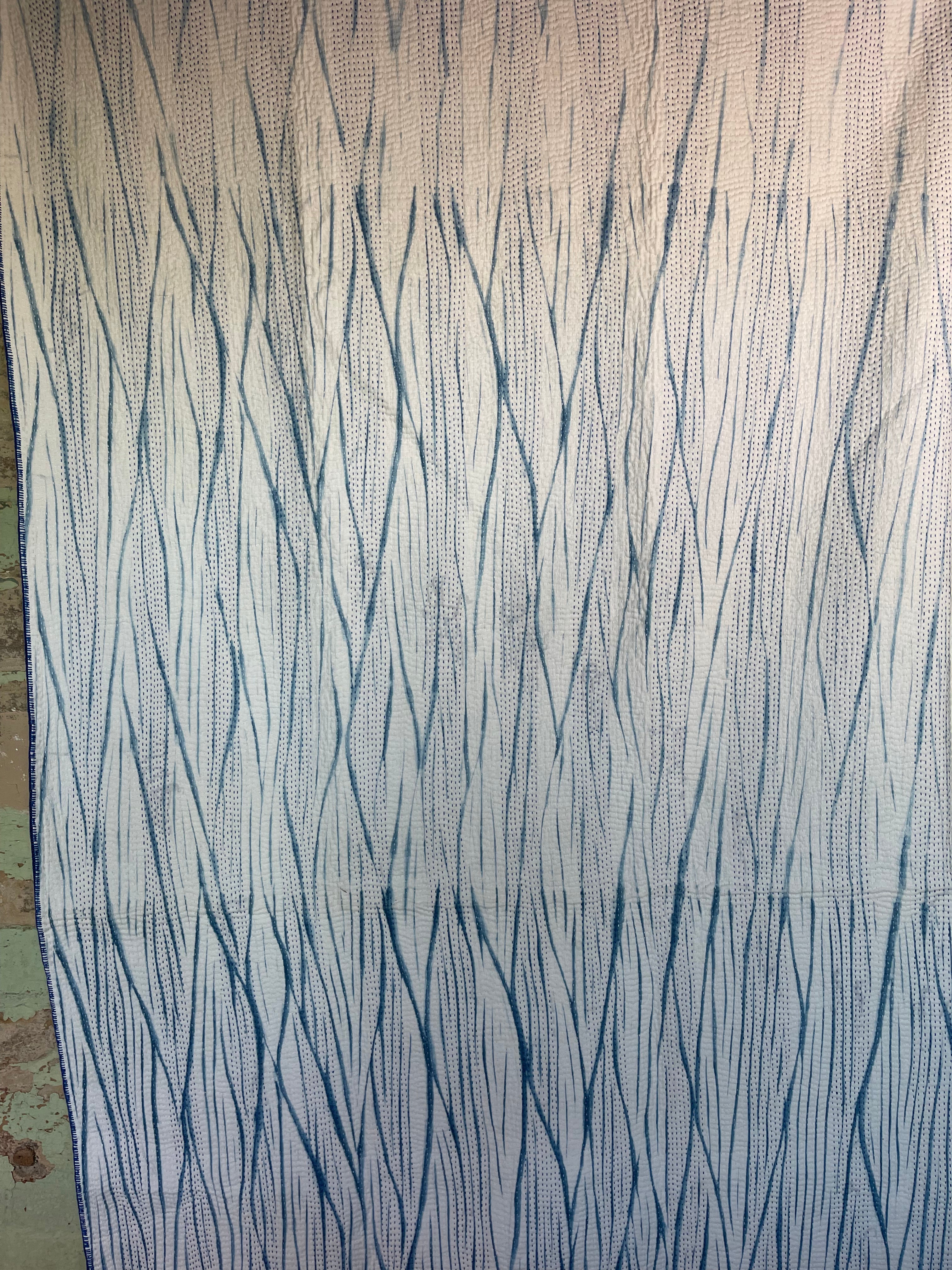 A sunningly beautiful indigo shibori kantha quilt, made by the artisans of LIVING BLUE. The front a graded vertical shibori pattern, in three diminshing panels of intensity of indiog blue; the reverse showing alternate fine white and blue hand stitiching resulting in a linear pattern of stripes - on a plain indigo background.