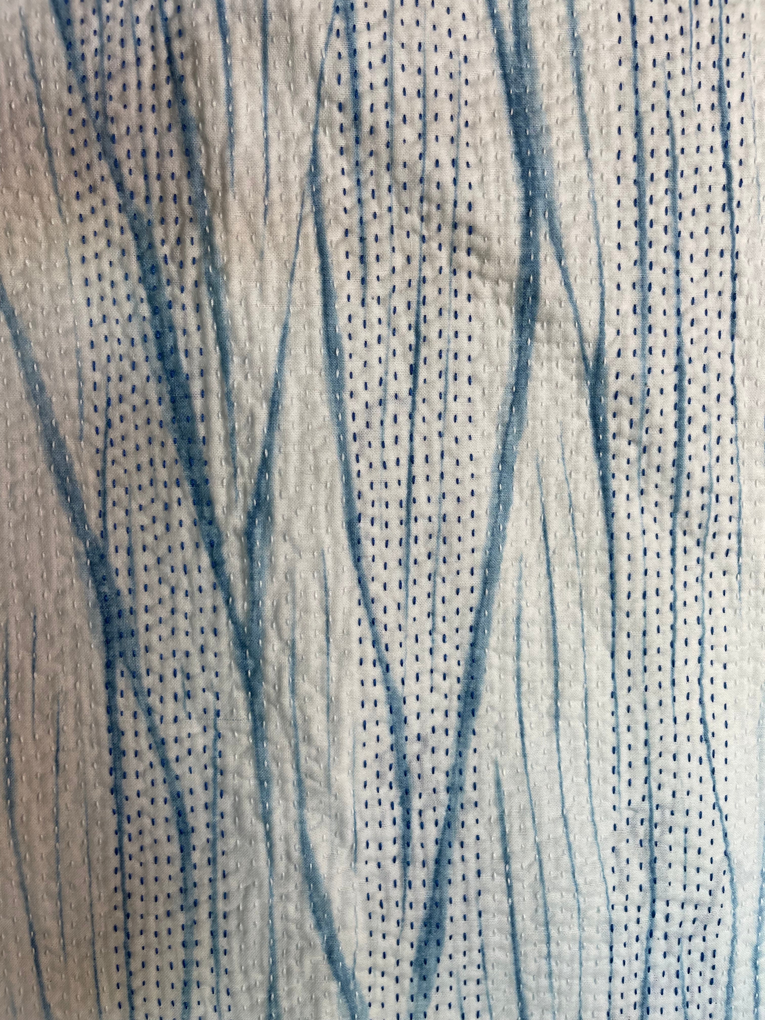 A sunningly beautiful indigo shibori kantha quilt, made by the artisans of LIVING BLUE. The front a graded vertical shibori pattern, in three diminshing panels of intensity of indiog blue; the reverse showing alternate fine white and blue hand stitiching resulting in a linear pattern of stripes - on a plain indigo background.