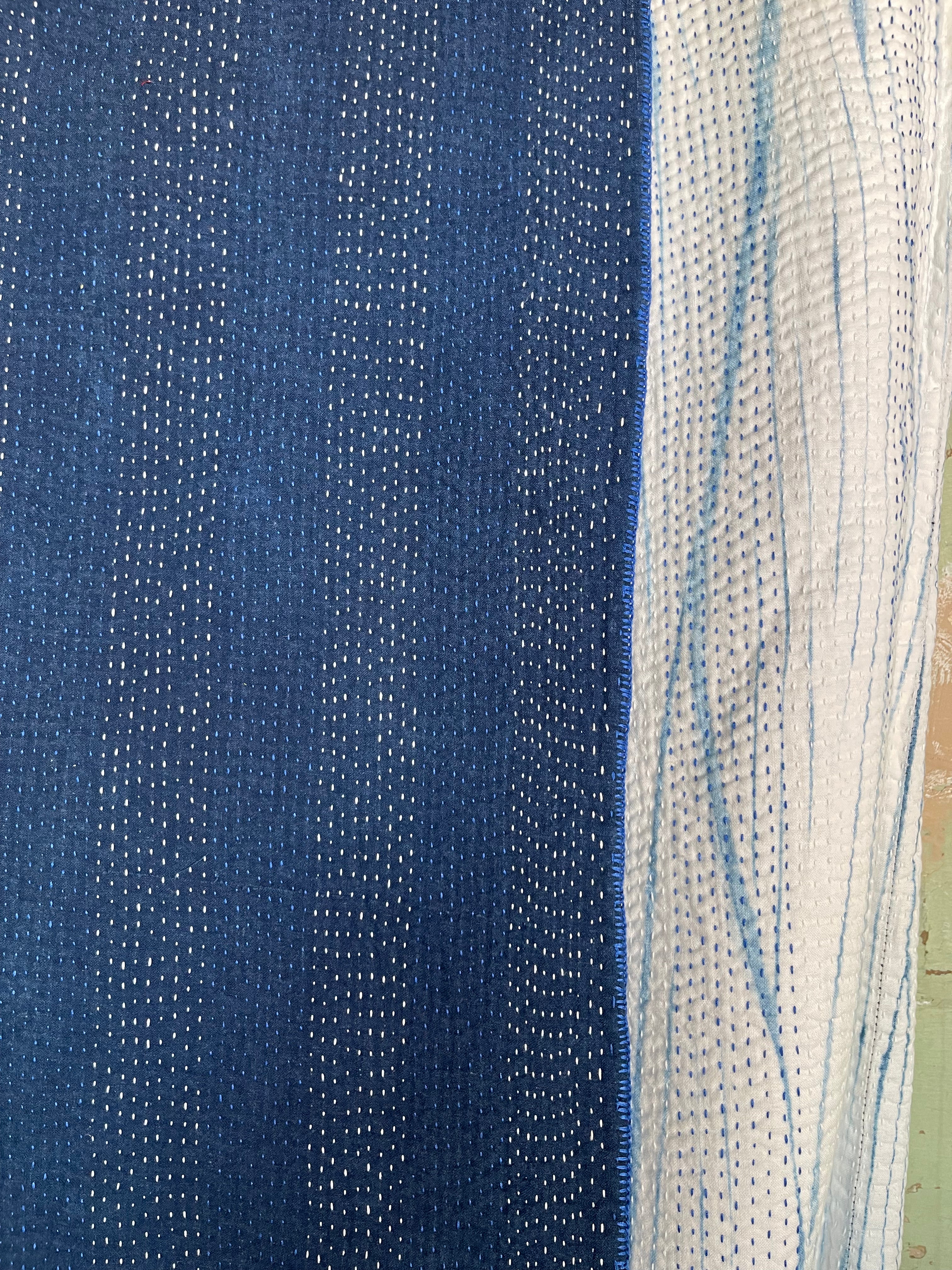 A sunningly beautiful indigo shibori kantha quilt, made by the artisans of LIVING BLUE. The front a graded vertical shibori pattern, in three diminshing panels of intensity of indiog blue; the reverse showing alternate fine white and blue hand stitiching resulting in a linear pattern of stripes - on a plain indigo background.