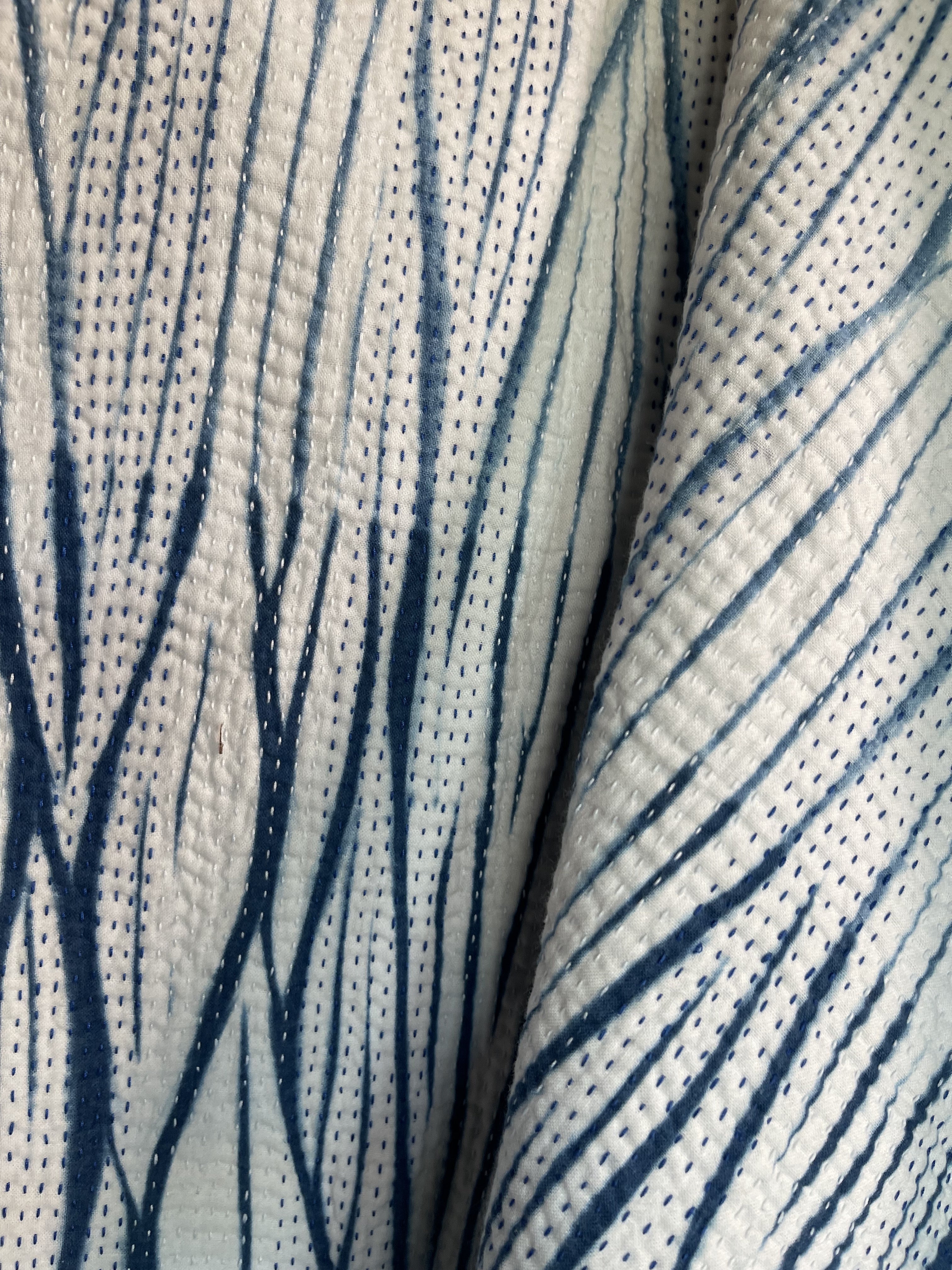 A sunningly beautiful indigo shibori kantha quilt,  made by the artisans of LIVING BLUE. The front a graded vertical shibori pattern, in three diminshing panels of intensity of indiog blue; the reverse showing alternate fine white and blue hand stitiching resulting in a linear pattern of stripes - on a plain indigo background.