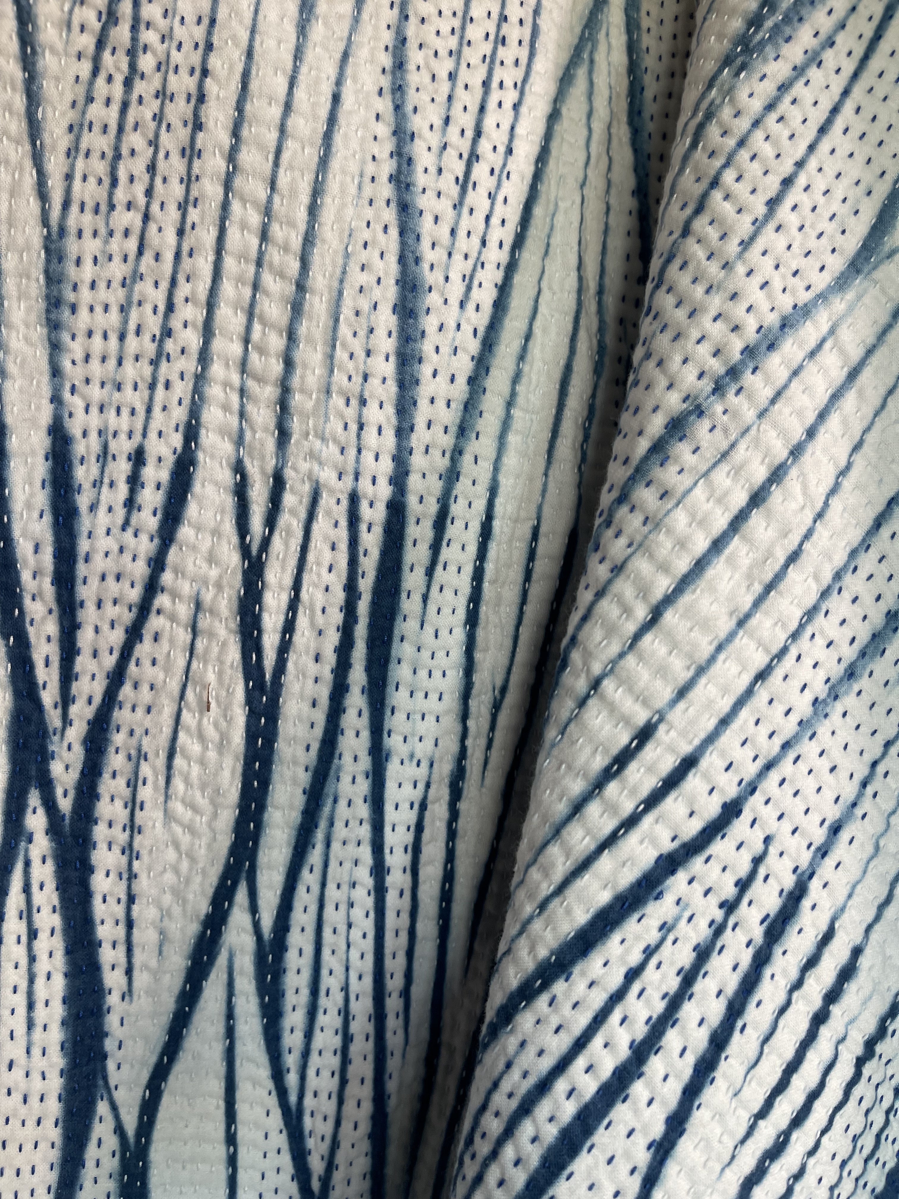A sunningly beautiful indigo shibori kantha quilt, made by the artisans of LIVING BLUE. The front a graded vertical shibori pattern, in three diminshing panels of intensity of indiog blue; the reverse showing alternate fine white and blue hand stitiching resulting in a linear pattern of stripes - on a plain indigo background.