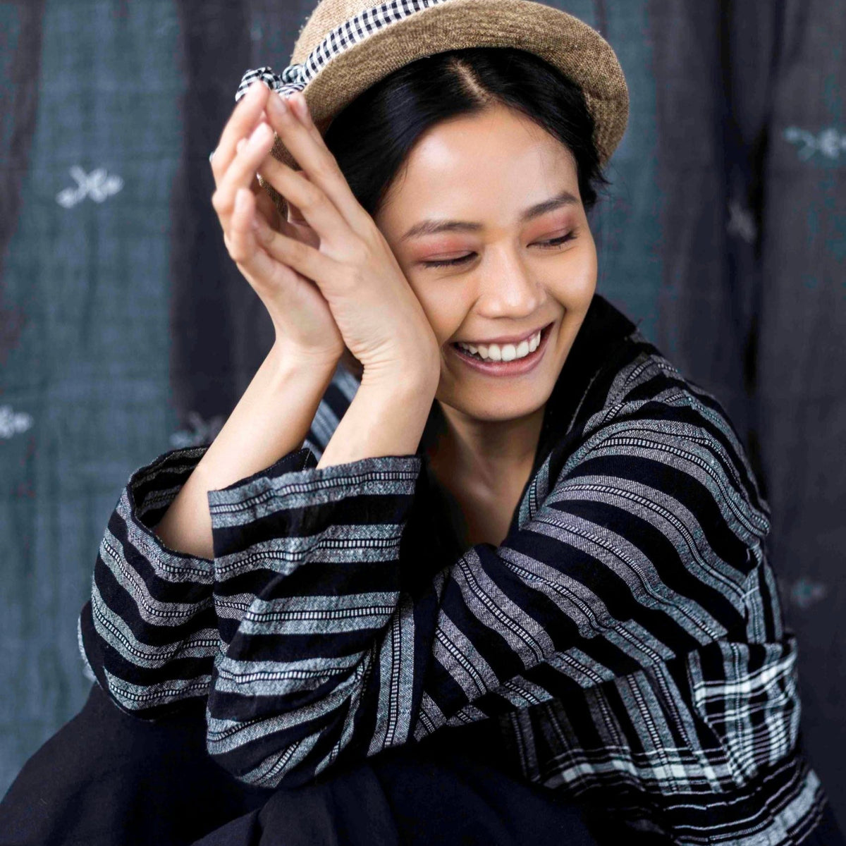 Woman wearing a striped sweater and hat against a dark curtain background