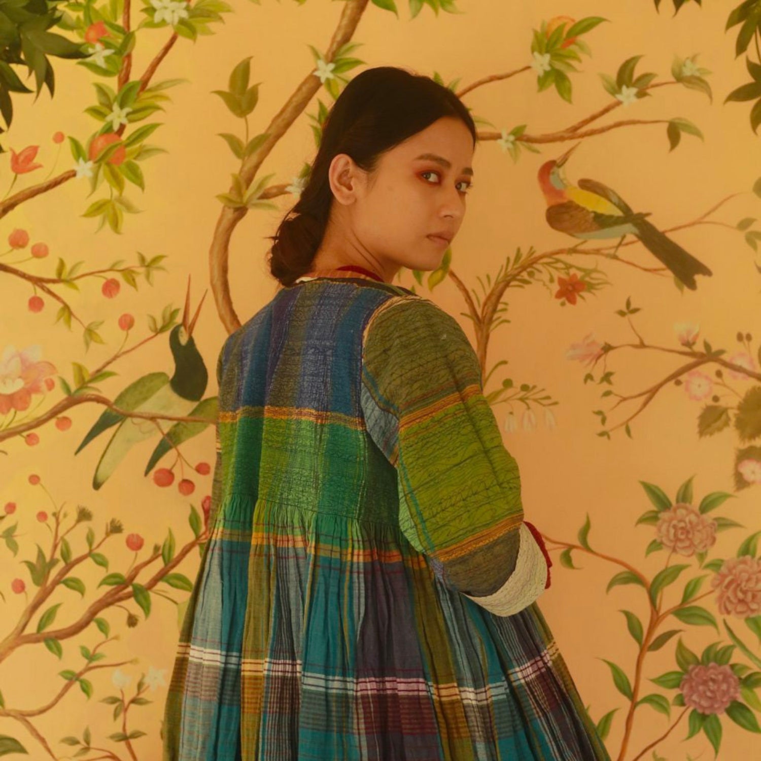 Woman in a colorful dress standing against a floral wallpapered wall.