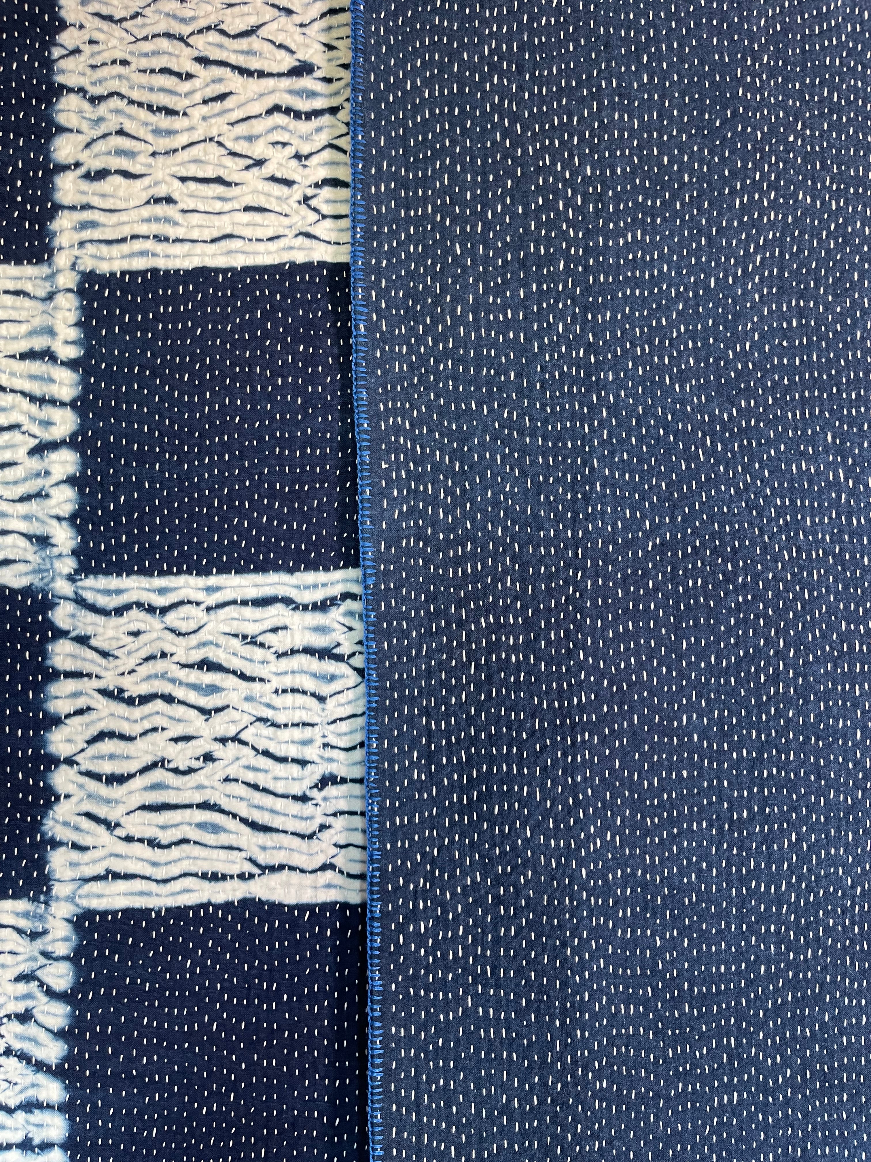 A sunningly beautiful indigo shibori kantha quilt,  made by the artisans of LIVING BLUE. The front a check pattern, the reverse showing fine white hand stitiching on a plain indigo background.