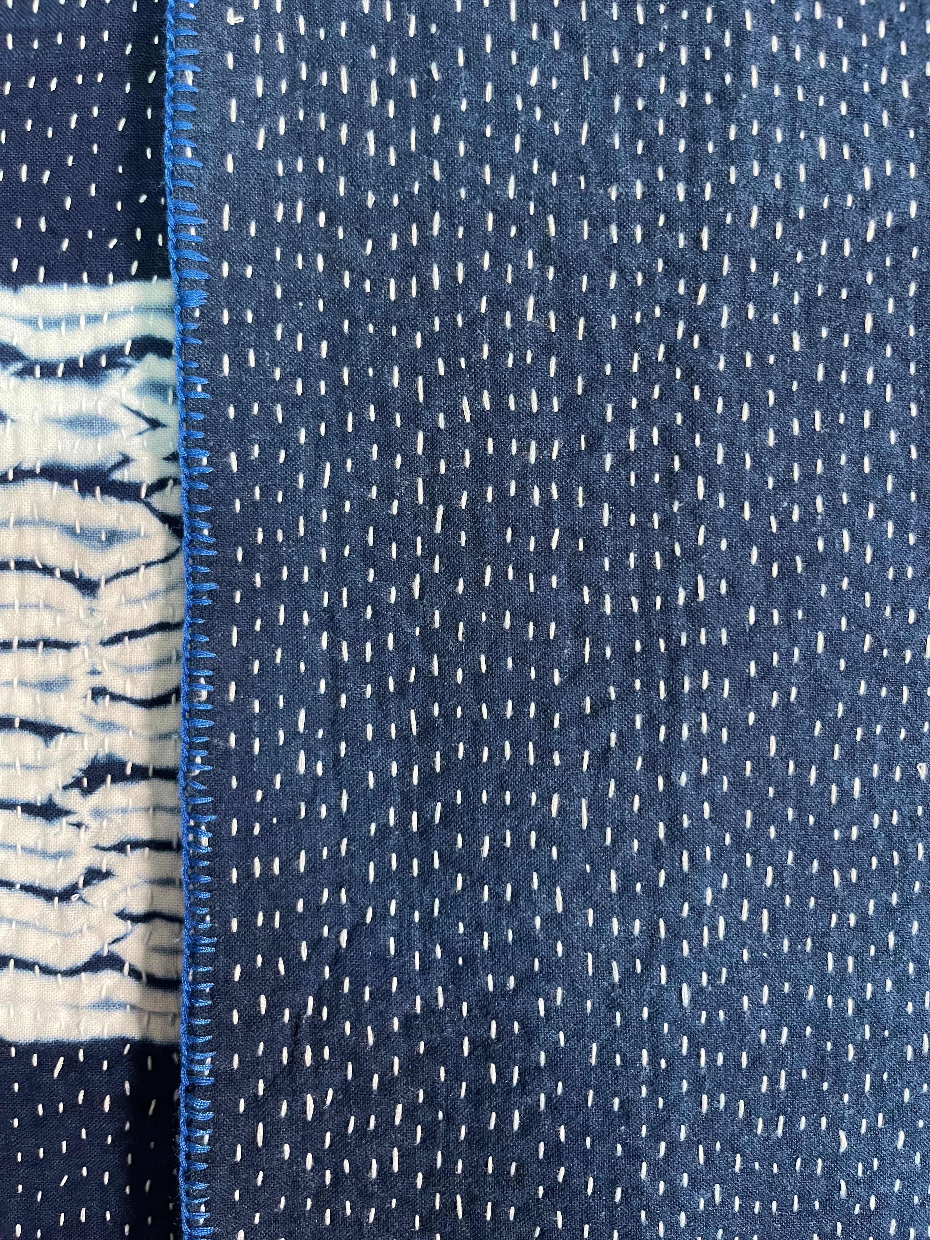 A sunningly beautiful indigo shibori kantha quilt,  made by the artisans of LIVING BLUE. The front a check pattern, the reverse showing fine white hand stitiching on a plain indigo background.